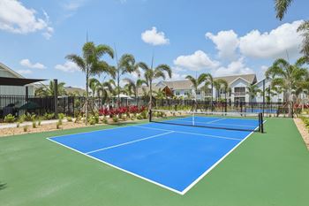 A blue tennis court surrounded by palm trees.